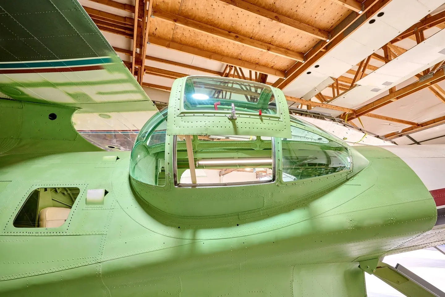 A green airplane in an air field with wooden ceiling.